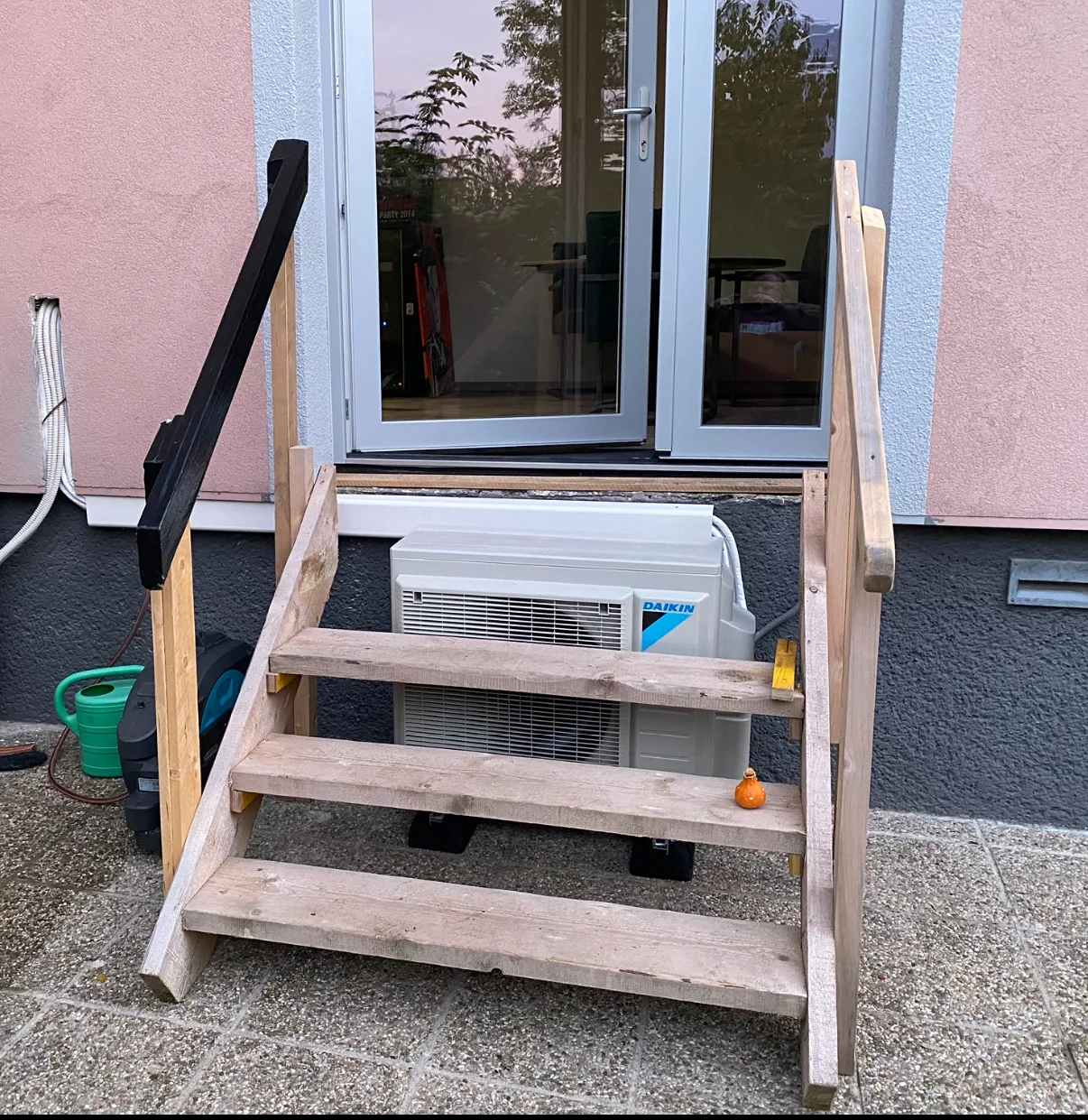 Daikin-Außengerät unter einer Holzstiege vor einer Terrassentür
